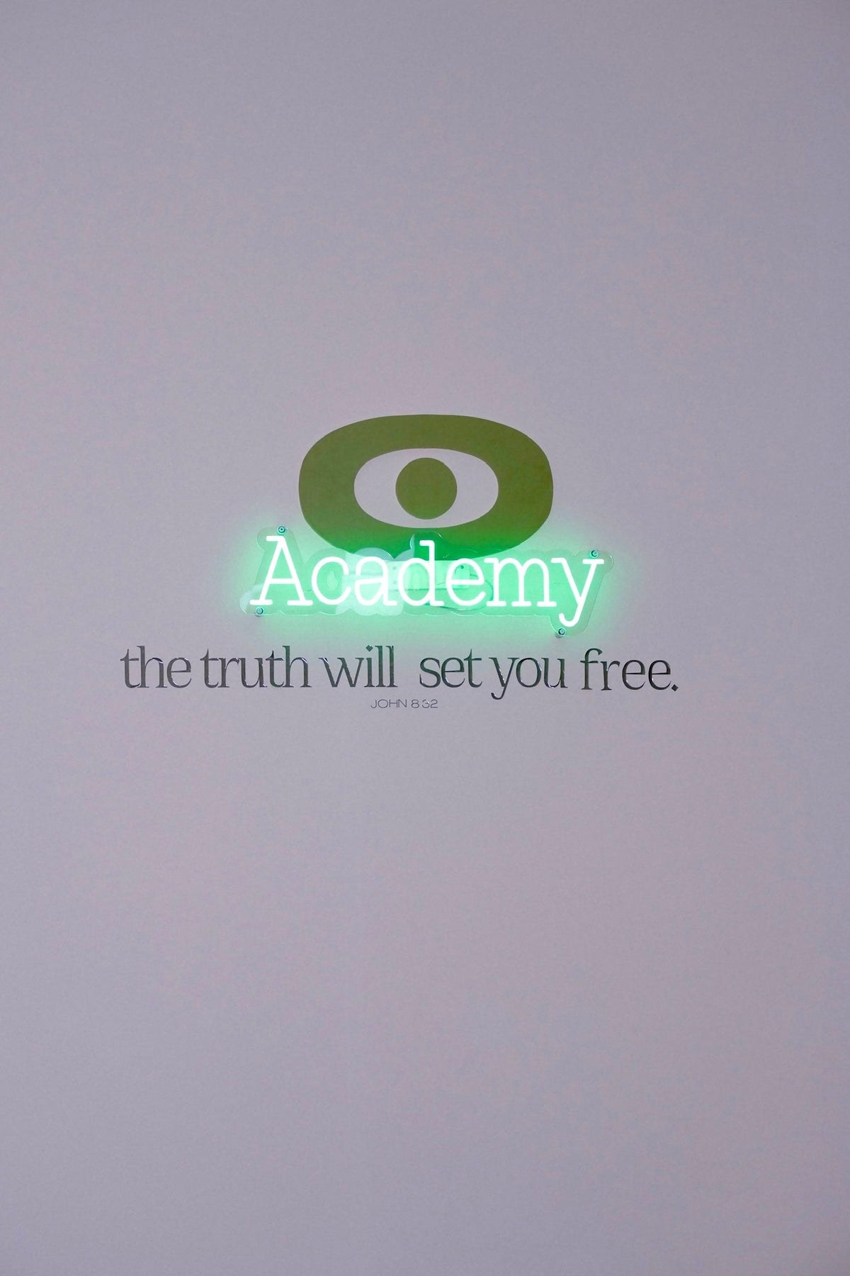 The eyeam Academy neon sign above the words the truth will set you free, on a white wall