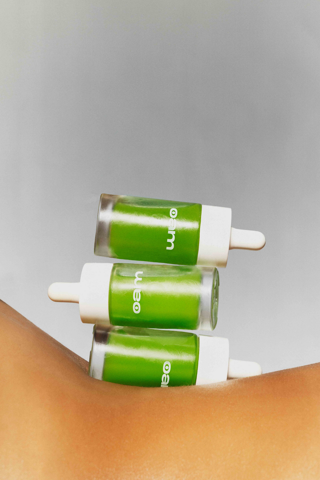 three green bottles of eyeam serum resting on tanned female skin