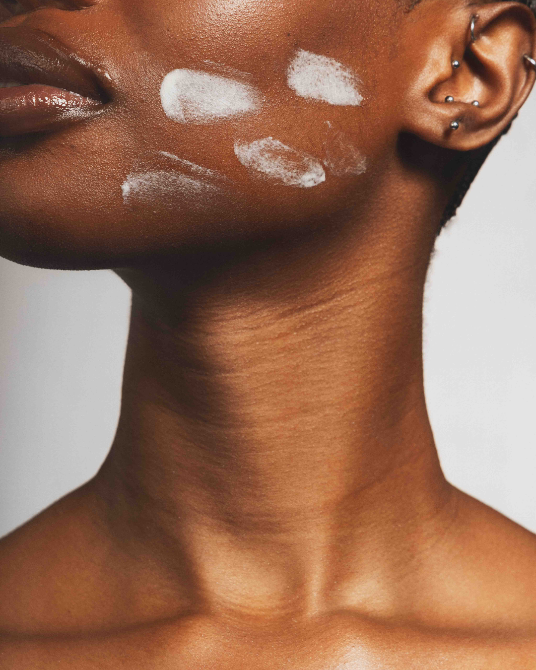 Close-up of model's face and neck with cream applied on her cheek.