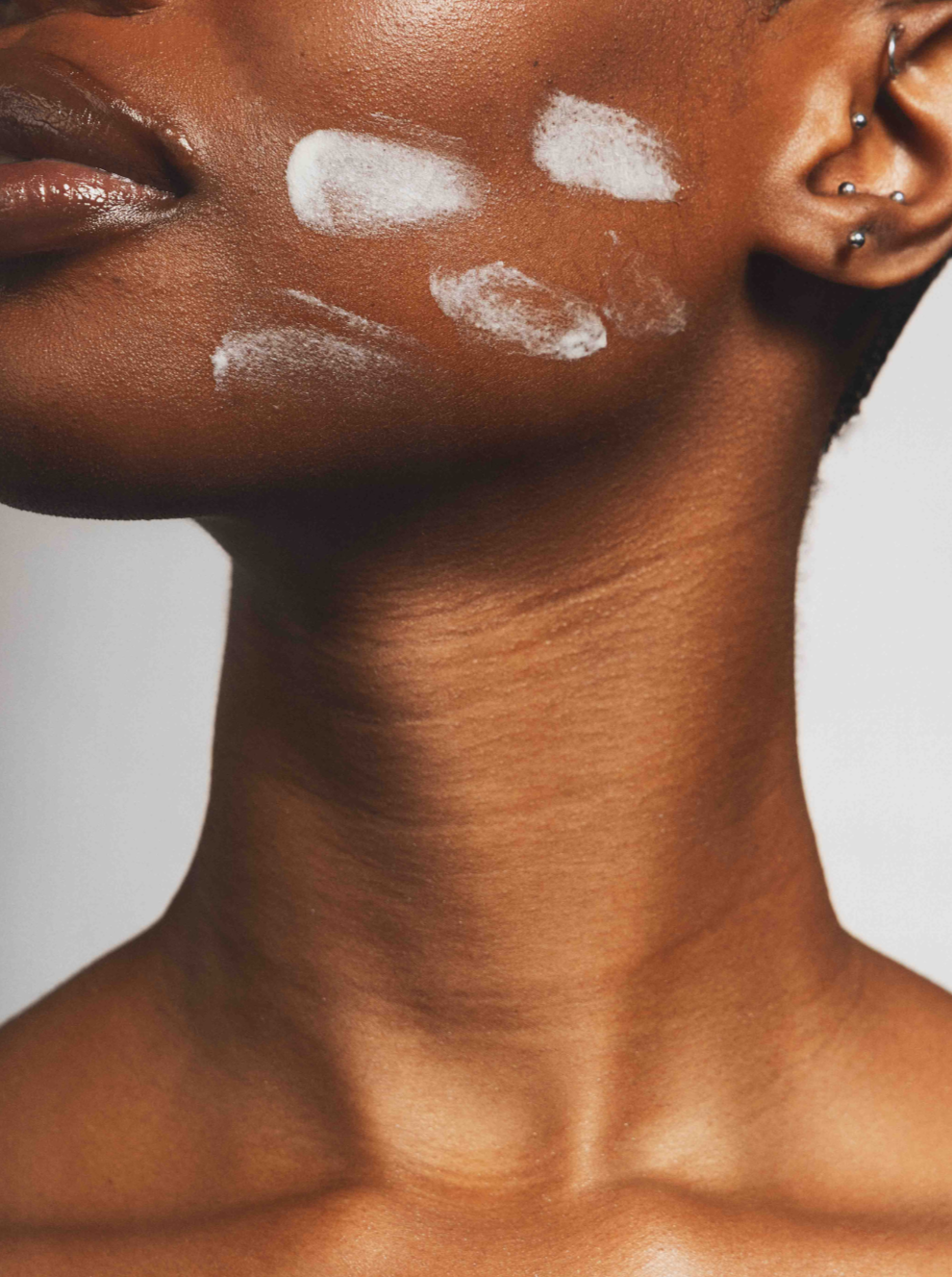 Close-up of model's face and neck with cream applied on her cheek.