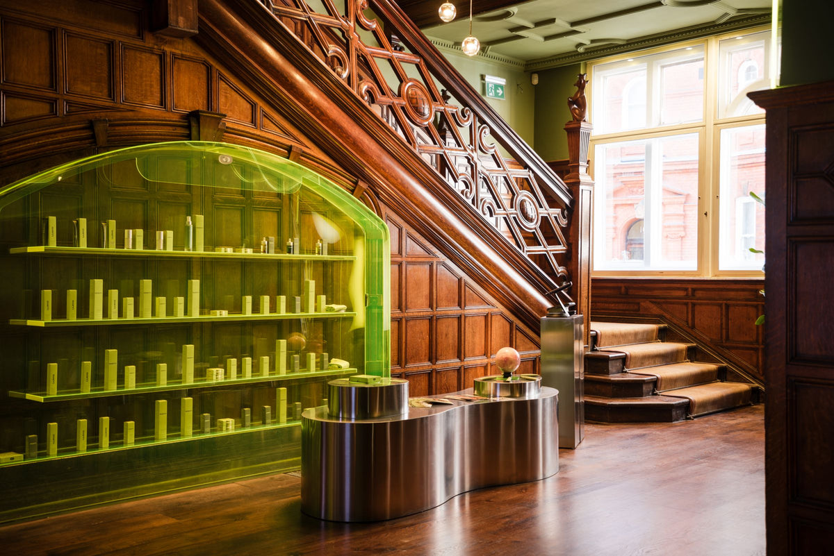 The entrance hall at eyeam world, 1 Cadogan Gardens: a wood-panelled staircase beside lime-lit shelves of eyeam products and a curved steel bench