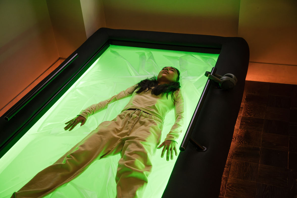 A guest lying back on the green-lit dry float bed in the eyeam spa